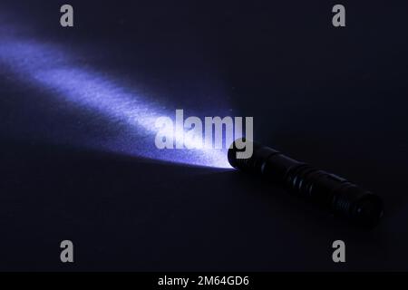 Taschenlampe und ein Lichtstrahl in der Dunkelheit. Eine moderne LED-Lampe mit heller Projektion auf einen dunklen Tisch. Oberfläche mit Kopierbereich. Stockfoto