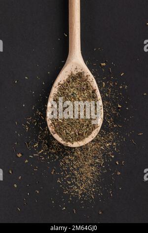 Getrockneter Oregano in Holzlöffel auf dunklem Hintergrund. Stockfoto