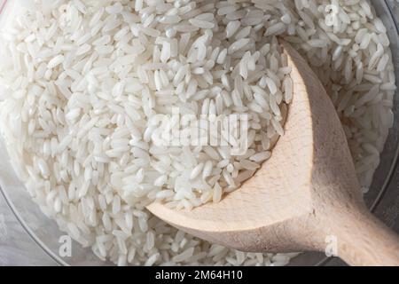 Trockener weißer Reis in Holzlöffel auf Reishintergrund. Stockfoto