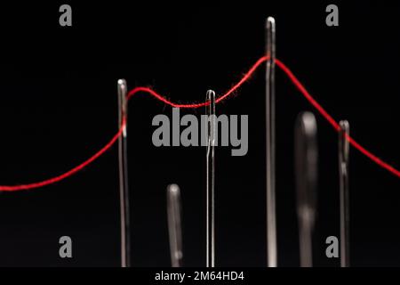 Roter Faden durch Nadeln auf schwarzem Hintergrund. Stockfoto