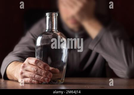 Ein betrunkener Mann, der seinen Kopf mit einer fast leeren Flasche Alkohol hält. Stockfoto