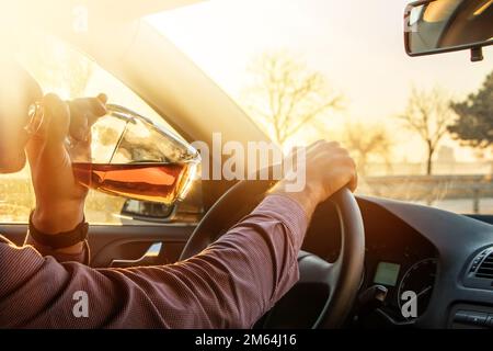 Ein Mann, der Alkohol trinkt, während er bei Sonnenuntergang im Auto fährt. Stockfoto