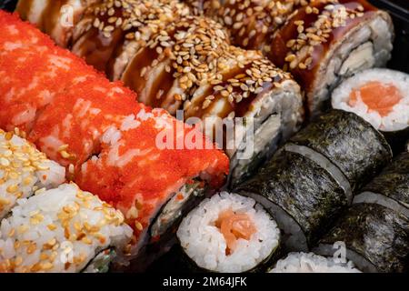 Japanisches Sushi. Maki und Brötchen mit Thunfisch, Lachs, Garnelen, Krabben und Avocado. Blick von oben auf verschiedene Sushi- und All-you-can-eat-Menüs. Regenbogen-Sushi-Brötchen Stockfoto