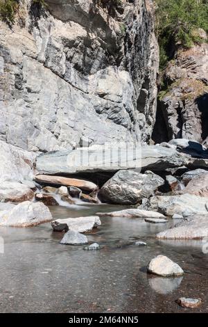 Lange Einwirkung von Wasser mit Nebel und kleinen Kieselsteinen, die durch den Lillaz-Wasserfall (Cascate di Lillaz) in Granitriss entstanden sind, vertikaler Schuss, Aosta-Tal, Italien Stockfoto