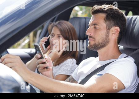 Ein Paar im Auto, das beide während der Fahrt Mobiltelefone benutzt Stockfoto