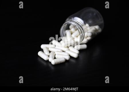 Weiße Pillen auf einem schwarzen Holztisch, Medikamente in Kapseln aus der Flasche verstreut. Hintergrund für Pharmazie, Antibiotika, Vitamine Stockfoto