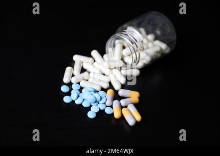 Verschiedene Pillen auf einem schwarzen Holztisch, Variation der Medikamente in Kapseln, die aus einer Flasche verstreut sind. Hintergrund für Pharmazie, Antibiotika, Vitamine Stockfoto