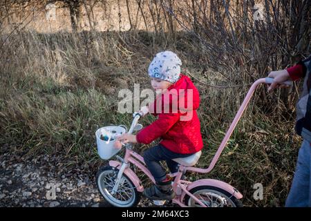 Ein kleines Mädchen auf einem Fahrrad fährt auf einer unbefestigten Straße. Ukrainischer Kindereinwanderer auf einer Spende eines gebrauchten Fahrrads durch eine Gastfamilie. Das kleine Kind lernt r Stockfoto