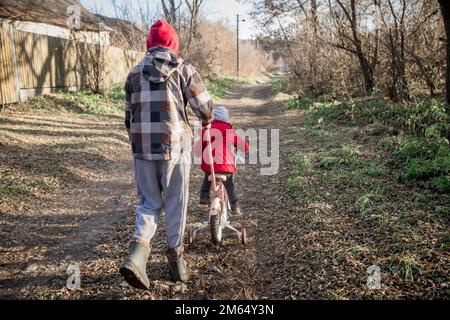 Der Bruder nimmt seine Schwester mit auf ein Fahrrad. Ukrainischer Kindereinwanderer auf einer Spende eines gebrauchten Fahrrads durch eine Gastfamilie. Stockfoto