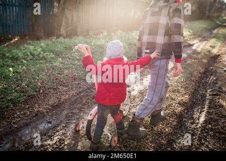 Ein Mädchen schiebt mit ihrem älteren Bruder ein Fahrrad. Kinder von Einwanderern haben Spaß im Dorf. Ein abgelegenes Dorf ohne Straßen. Ukrainische Kindermov Stockfoto