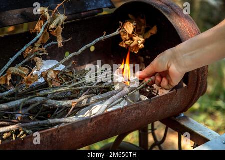 Bereiten Sie ein Barbecue zum Kochen in der Natur zu. Anzünden mit Streichpapier zum Verbrennen von Holz. Hohe Verbrennungstemperatur. Schließen. Stockfoto