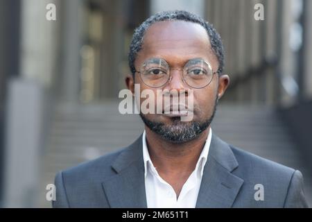 Nahaufnahme eines seriösen Geschäftsmanns, afro-amerikanischer Mann in Business-Anzug und Brille, der in Kameradenken schaut, Boss außerhalb des Bürogebäudes. Stockfoto