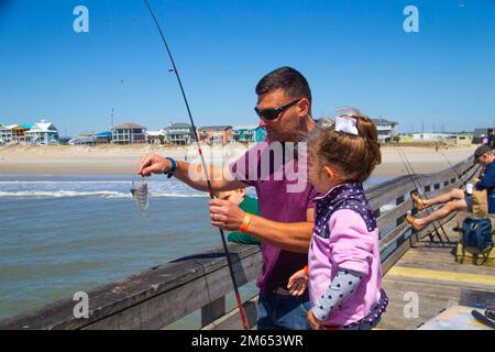 USA Leitender Petty Officer der Küstenwache Paul Rabczak mit der Küstenwache in Fort Macon und seiner Tochter fangen einen Fisch während eines Family Fishing Day, der vom Carteret County Chamber of Commerce Military Affairs Committee (MAC) am Oceana Fishing Pier, Atlantic Beach, North Carolina, am 2. April 2022 ausgerichtet wird. Der MAC richtete diese Veranstaltung aus, um dem Militär und seinen Familien für ihren Dienst zu danken. Stockfoto