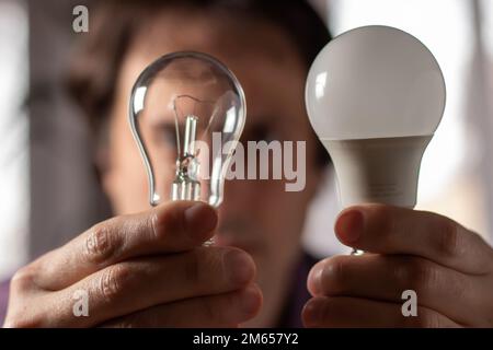 Zwei Lampen in den Händen eines Mannes. Glühlampe und LED-Lampe in Ihren Händen. Nahaufnahme. Stockfoto