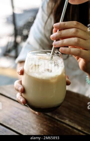 Eiskaffee in der Hand. Ein Glas kalten Kaffeegetränks mit Milch in der Hand eines Mädchens in einem Sommerkaffee auf der Straße. Drink, Lifestyle, Stadtkonzept. Hochwertiges Foto Stockfoto