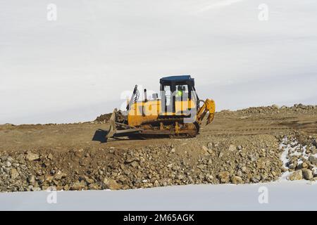 Unerkannter Arbeiter, der im Winter auf Straßenbaustellen in den Zlatibor Hills Schwerlastmaschinen mit industriellem Bulldozer fährt Stockfoto