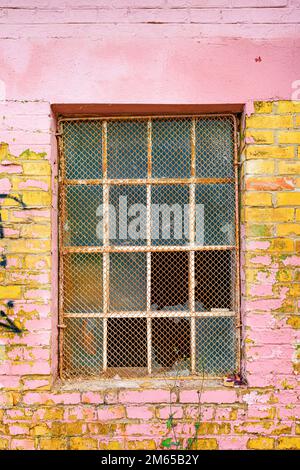 Alte Gitterfenster mit zerbrochenem Glas an der Außenwand eines alten verlassenen Fabriklagers Stockfoto