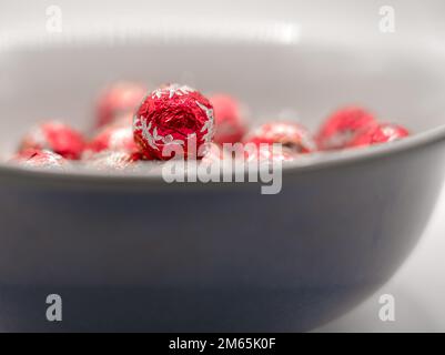 Eine blaue Schüssel gefüllt mit roter Folie verpackte weihnachtsschokoladen-Kugeln Stockfoto