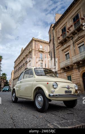 Ein vertikales Bild eines cremefarbenen Fiat 500 Autos auf einer Straße in Syracuse, Sizilien Stockfoto