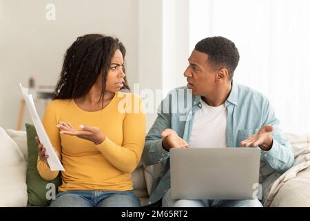 Wütendes, trauriges, afroamerikanisches Millennials-Paar streitet sich um Schulden und Rechnungen mit Papieren und Laptop im Wohnzimmer Stockfoto
