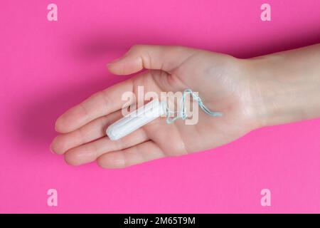 Junge Frau hält Menstruationstampon in der Hand - weibliche Menstruationskrämpfe. Menstruation, Schutzmittel. Stockfoto