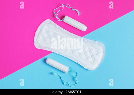 Damenpolster und Tampon – Hygienepads liegen neben einem Tampon auf einem isolierten Hintergrund auf einem pinkfarbenen und blauen Hintergrund. Frauenhygiene und Menstruation per Stockfoto