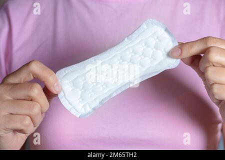 Ein Mädchen, das sich in der Hand hält, ein Hygienepad auf rosa Hintergrund. Stockfoto