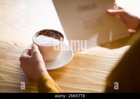 Eine unbekannte Frau, die Zeit im Café verbringt, Kaffee trinkt, die Speisekarte liest Stockfoto