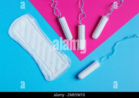 Damenpolster und Tampon – Hygienepads liegen neben einem Tampon auf einem isolierten Hintergrund auf einem pinkfarbenen und blauen Hintergrund. Frauenhygiene und Menstruation per Stockfoto