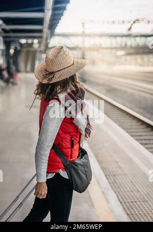 Nahaufnahme einer weiblichen Touristen mit Hut, am Bahnhof, die auf die Schienen wartet. Konzeptwochenende und Geschäftsreise. Stockfoto