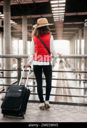 Allgemeiner Blick auf eine Reisende Frau, deren Rücken gedreht ist und die sich auf einem Geländer lehnt und den Bahnhof von oben beobachtet. Reisen und Unterhaltung Stockfoto