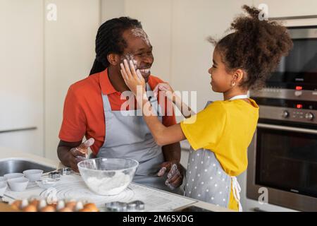 Fröhliches Schwarzes Mädchen Spielt Mit Dad In Kitchen, Während Sie Zusammen Backen Stockfoto