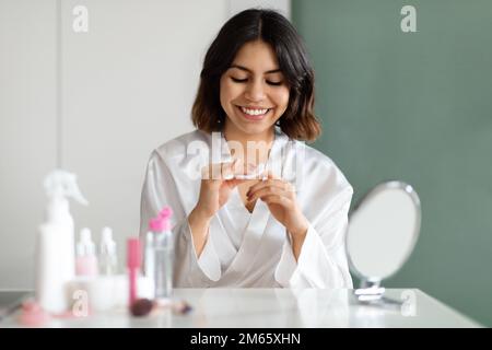 Eine Frau aus dem Nahen Osten im weißen Bademantel, die zu Hause Maniküre macht Stockfoto