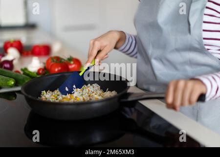 Weibliche Hände mischen Reis mit Gemüse in der Bratpfanne Stockfoto