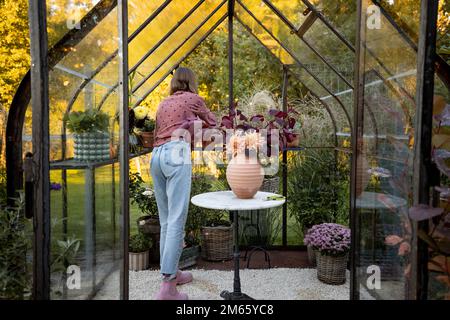 Frau Floristin macht einen schönen Blumenstrauß im Gewächshaus im Hinterhof Stockfoto