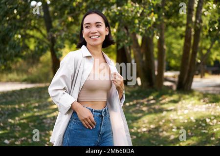 Das stilvolle asiatische Mädchen geht im Park spazieren, lacht und genießt das Sommerwetter. Menschen- und Lifestyle-Konzept Stockfoto