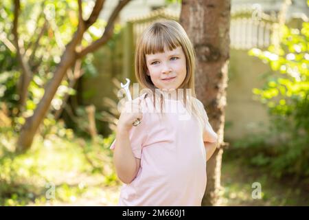 Junge Frau, Kind im Grundschulalter, posiert mit einem kleinen Metallschlüssel, Außenaufnahme, Porträt, eine Person. Mechaniker, Jobs, Berufe, Freiheit Stockfoto