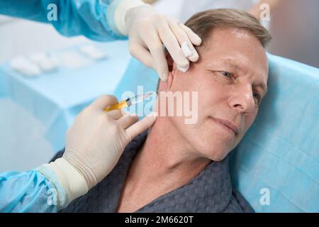 Erwachsener Mann, der während der medizinischen Injektion erfreut aussah Stockfoto