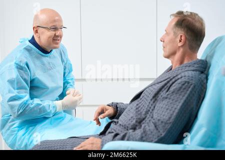 Gütiger männlicher Sanitäter, der mit seinem Patienten spricht Stockfoto