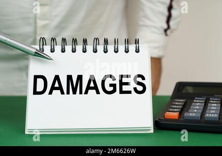 Geschäftskonzept. Auf einer grünen Oberfläche befindet sich ein Taschenrechner, ein Mann zeigt mit einem Stift auf ein Notizbuch mit der Aufschrift - Schäden Stockfoto