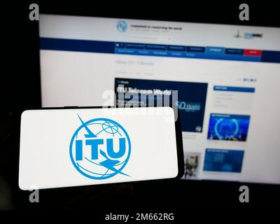 Person, die ein Smartphone mit dem Logo der Internationalen Fernmeldeunion (ITU) auf dem Bildschirm vor der Website hält. Konzentrieren Sie sich auf das Display des Telefons. Stockfoto