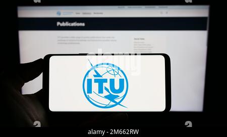 Person, die ein Mobiltelefon mit dem Logo der Internationalen Fernmeldeunion (ITU) auf dem Bildschirm vor der Webseite hält. Konzentrieren Sie sich auf das Display des Telefons. Stockfoto