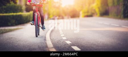 Ein Junge, der mit dem Fahrrad auf dem Bürgersteig entlang der Asphaltstraße fährt. Stockfoto