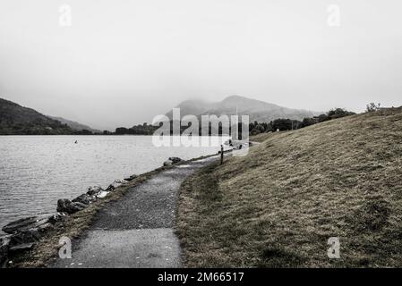 Wandern Sie entlang des Sees mit Bergen im Hintergrund in dramatischem Stil Stockfoto