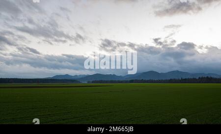 Wunderschöne grüne Landschaft mit Ackerland und Bergen in der Ferne unter einem dramatisch bewölkten Himmel. Stockfoto
