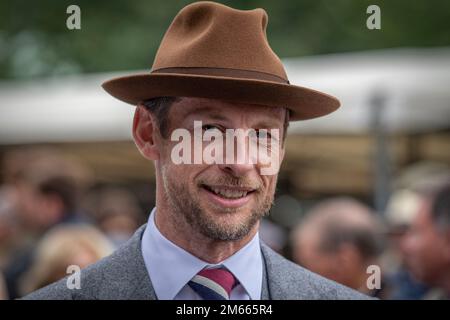 F1 Weltmeister Jenson Button lächelt im Goodwood Revival in antiker Kleidung und Hut Stockfoto