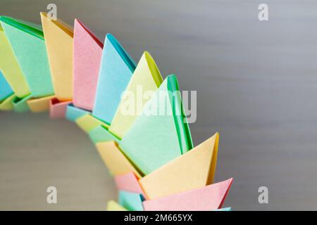 Farbenfroher Origami-Ring auf weißem Tischhintergrund, abstrakte parametrische Struktur aus Papierblättern, Nahaufnahme mit selektivem Weichzeichner Stockfoto