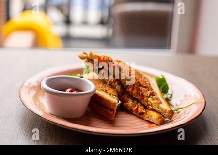 Gebratenes Club Sandwich mit Fleisch, Schinken, Käse, Grünzeug, Eiern, Aufgeteilt in zwei Stücke, serviert auf einem Teller und Ketchup-Sauce Stockfoto