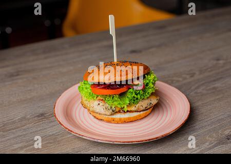 Nahaufnahme von leckeren frischen Hamburgern mit Spieß auf dem Teller im Restaurant. Rindfleisch, Schweinefleisch oder gegrillter Hähnchenburger auf einem Holztisch Stockfoto