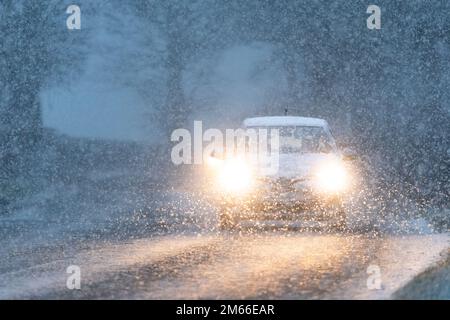 Autofahrt im Schnee am frühen Morgen mit eingeschalteten Scheinwerfern – Schottland, Großbritannien Stockfoto